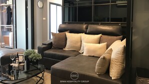 A modern living room with a leather sofa, a glass coffee table, and a large window. - Stay in Style The Heart of Nimman R306A (Chiang Mai)