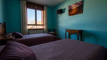 A room with two beds, a window with curtains, a TV mounted on the wall, and a painting.