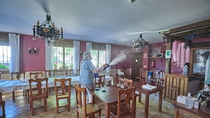 A dining area with wooden tables and chairs, a chandelier, and a person using a spray device. - Hotel Rural Tirontillana (Cuellar)