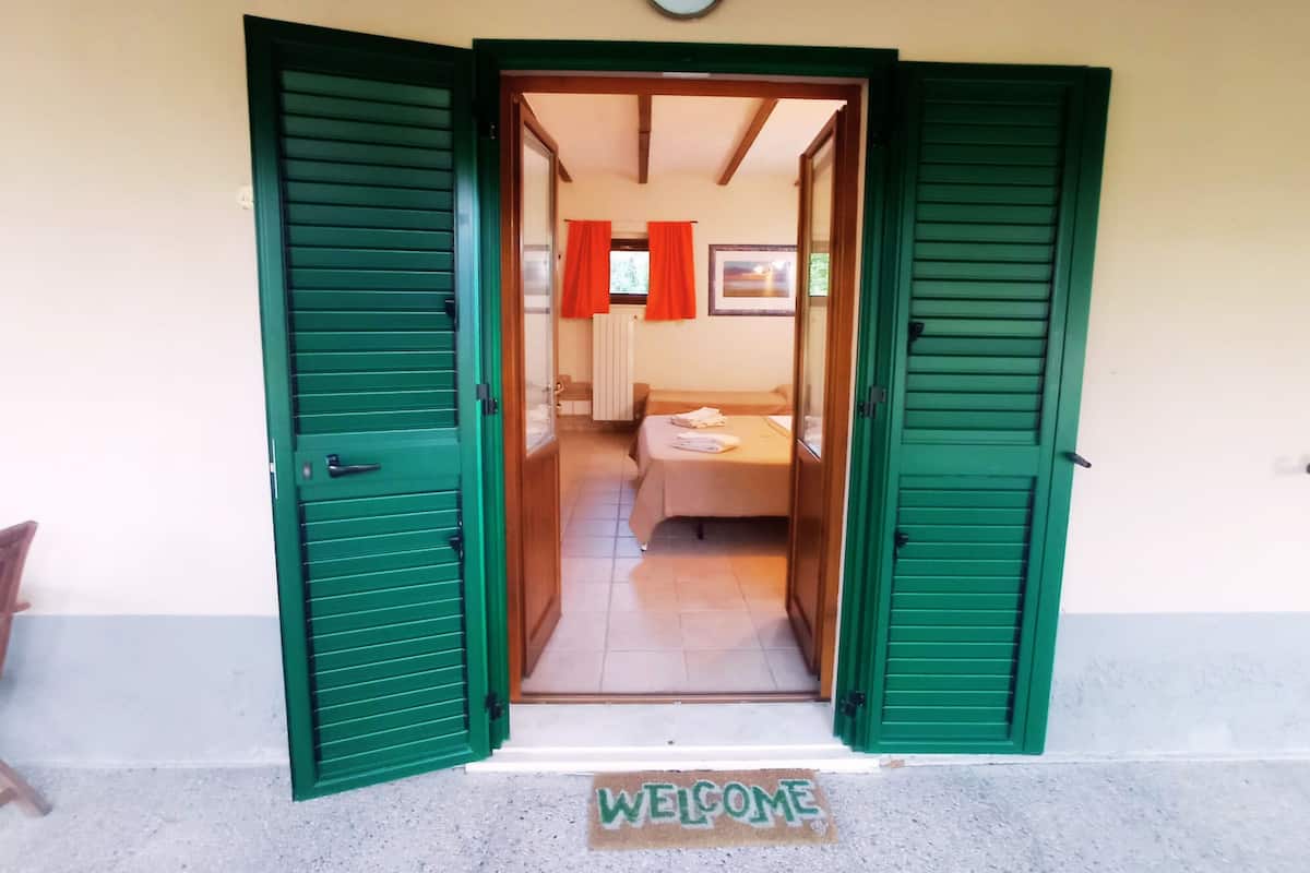 A doorway with green shutters, a bed, a radiator, and a framed picture on the wall.