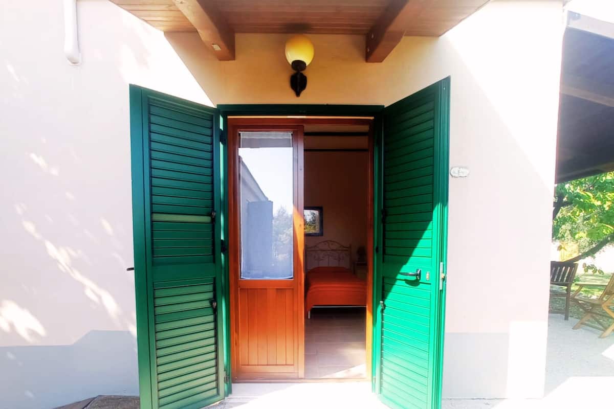 A room with a bed, a window, and a door with green shutters.