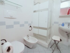Bathroom features a toilet, bidet, glass shower enclosure, and a sink with a soap dispenser.