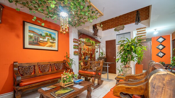 A room with a wooden bench, a wooden table with a book and a plant, and a large potted plant. - Ayenda 1422 Caney (Cali)