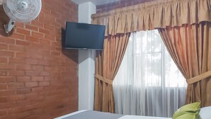 A hotel room with a brick wall, a mounted TV, a bed with a grey mattress, and beige curtains. - Ayenda 1422 Caney (Cali)