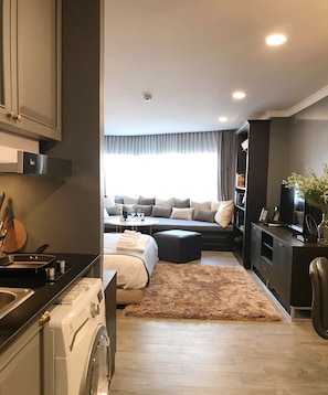 A modern kitchen with a washing machine, a dining area with a table and chairs, a sofa, and a TV.