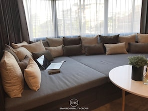 A modern living room with a grey sectional sofa, multiple cushions, a laptop, and a small table with a plant.