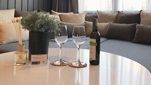 Un salon moderne avec une table ronde blanche, deux verres à vin, une bouteille de vin, une plante en pot et un petit flacon de parfum.