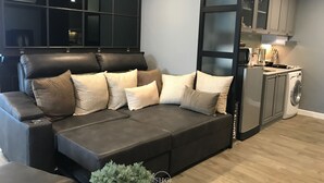 Un salon moderne avec un canapé d’angle, un meuble de rangement intégré pour les appareils électroniques et un coin buanderie.