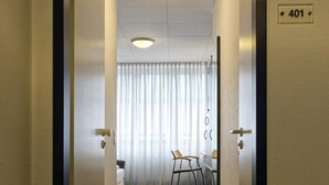 A hallway with a door labeled "401" leading to a room with a bed, a chair, and a table. - Opera Hotel Köln (Cologne)