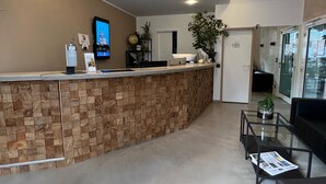 A reception area with a wooden reception desk, a flat-screen TV, a potted plant, and a glass coffee table. - Opera Hotel Köln (Cologne)
