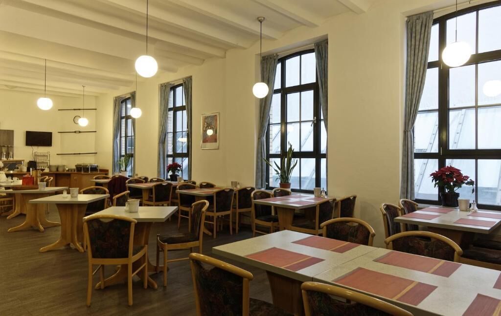 A dining area with multiple tables and chairs, large windows with curtains, and hanging pendant lights.