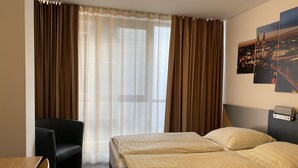 A hotel room with a bed, a desk, a chair, and a window with curtains. - Opera Hotel Köln (Cologne)