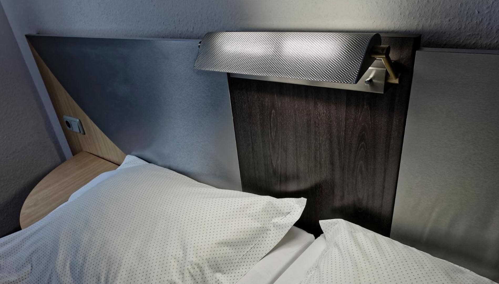 A compact bed with white linens in a room with a wooden headboard and a textured wall.