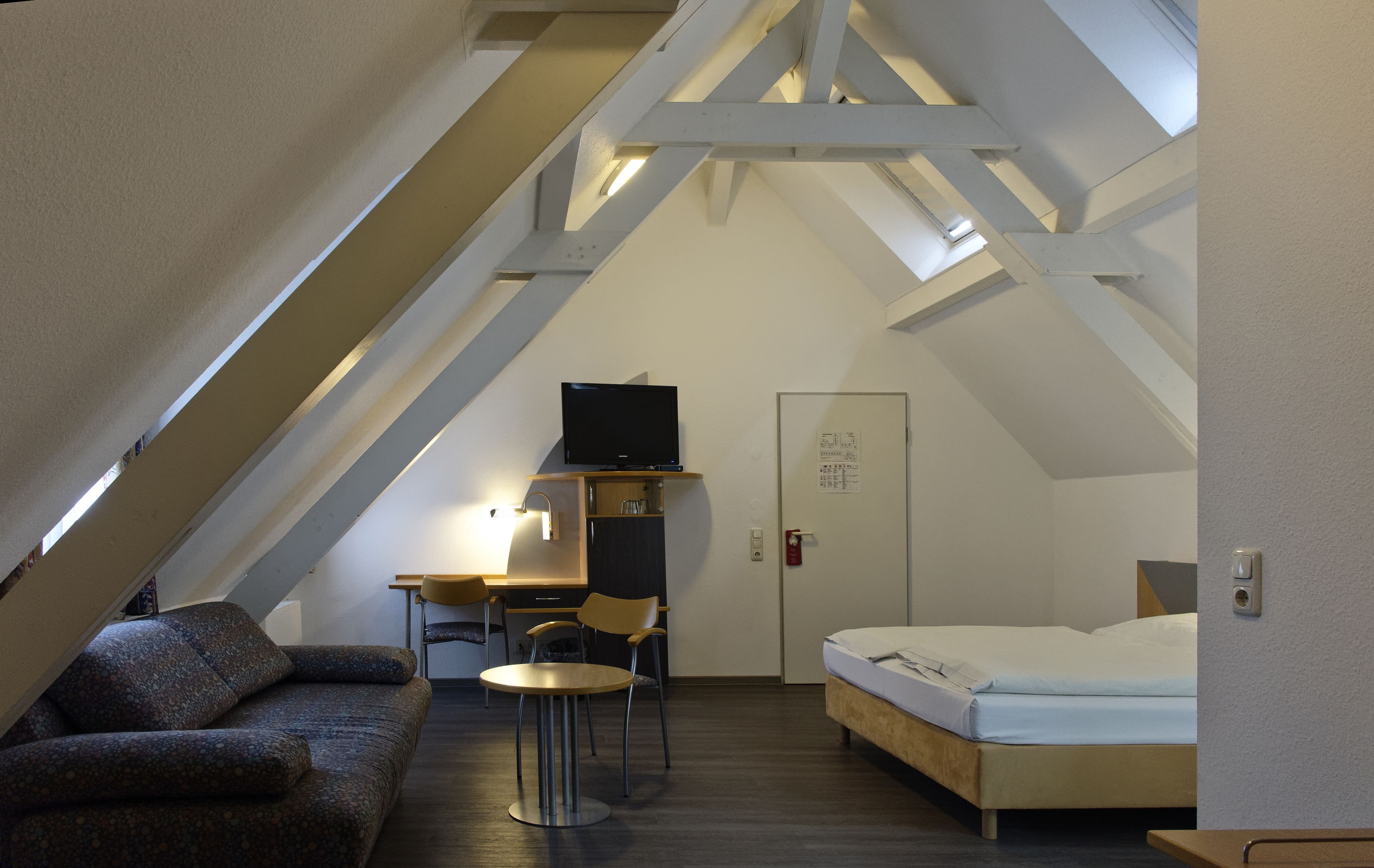 Una stanza moderna e accogliente con soffitto a falde, un letto, un divano, una scrivania e una sedia.