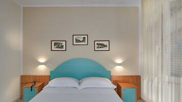 A bedroom with a teal headboard, two bedside tables, a bed with white bedding, and three framed pictures on the wall.