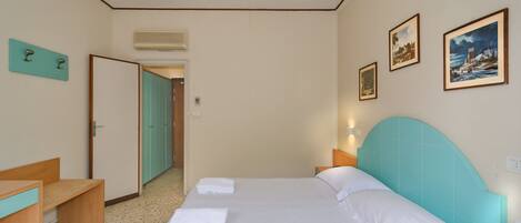 A hotel room with a bed, a desk, a bench, and a door leading to another room.