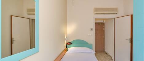 A single-bed room with a large mirror, a wooden headboard, a bedside table, and a small desk.