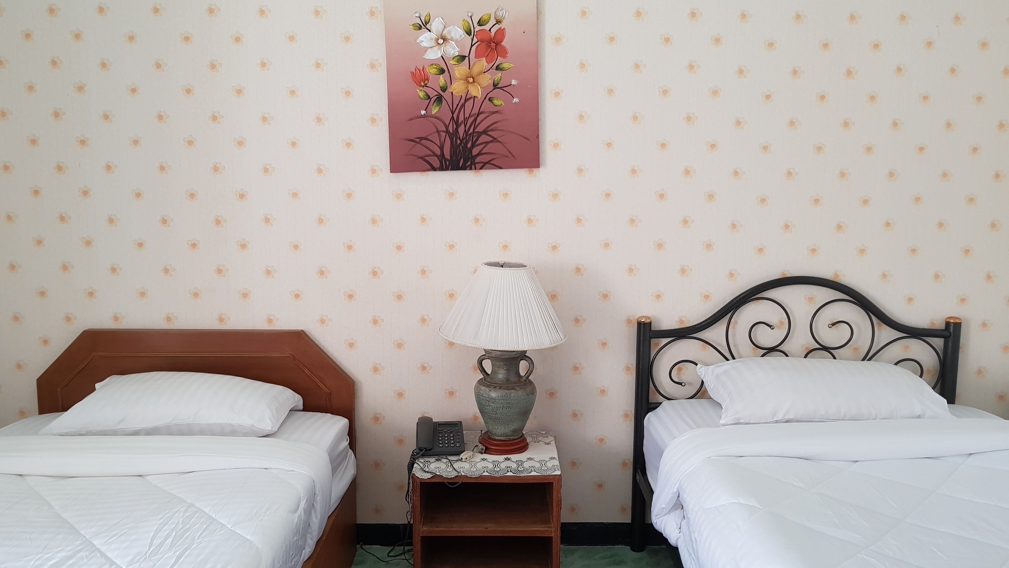 Une chambre avec deux lits, une table de chevet avec une lampe et une œuvre d’art aux motifs floraux accrochée au mur.