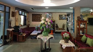 A cozy living room with a large green vase, a sofa, and a table with a floral tablecloth. - Wiang Inn Mansion (Chiang Mai)