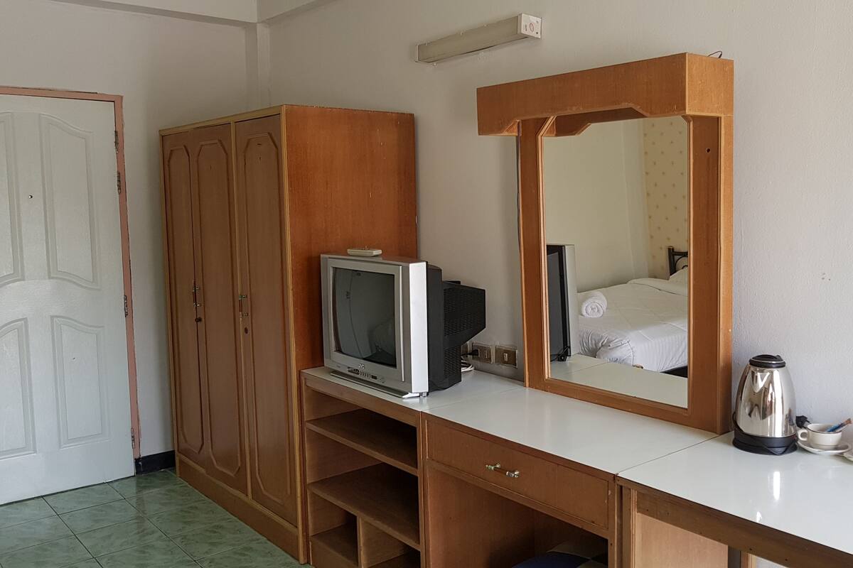 A hotel room with a wooden wardrobe, a television on a white table, a large mirror, and a coffee maker.