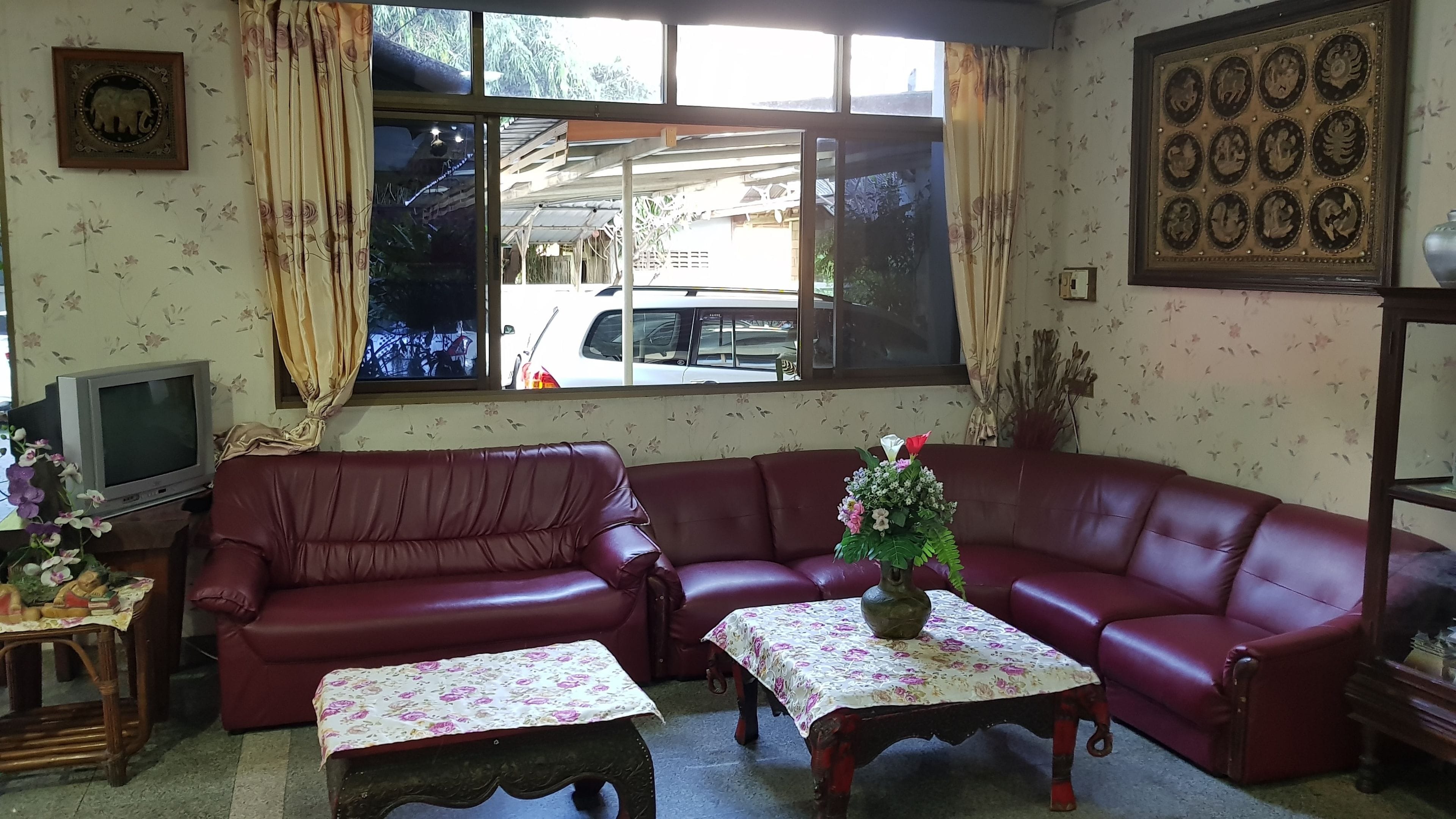 A living room with a red leather sofa, two matching tables, a television, and a large window with a view of the street.