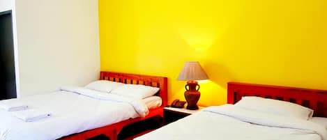 Habitación de hotel con dos camas individuales, una mesita de noche con lámpara y una pared amarilla lisa.