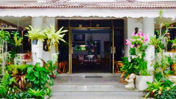 A building with a tiled roof and a central entrance with glass doors. There are potted plants and a statue on either side of the entrance. - Wiang Inn Mansion (Chiang Mai)