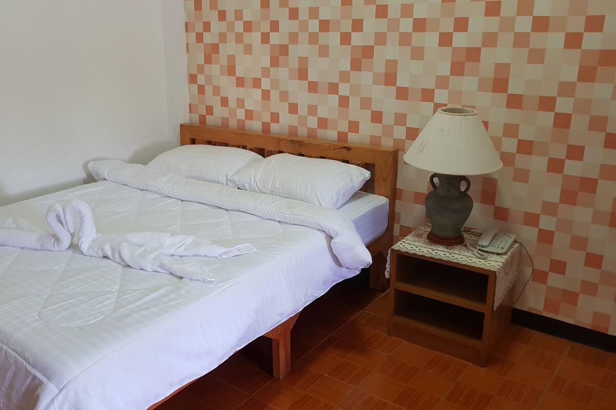 A neatly made bed with white linens and a towel arranged in a heart shape.