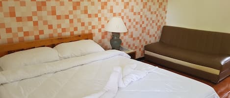 A neatly made bed with white linens, a brown sofa, and a checkered wall pattern.