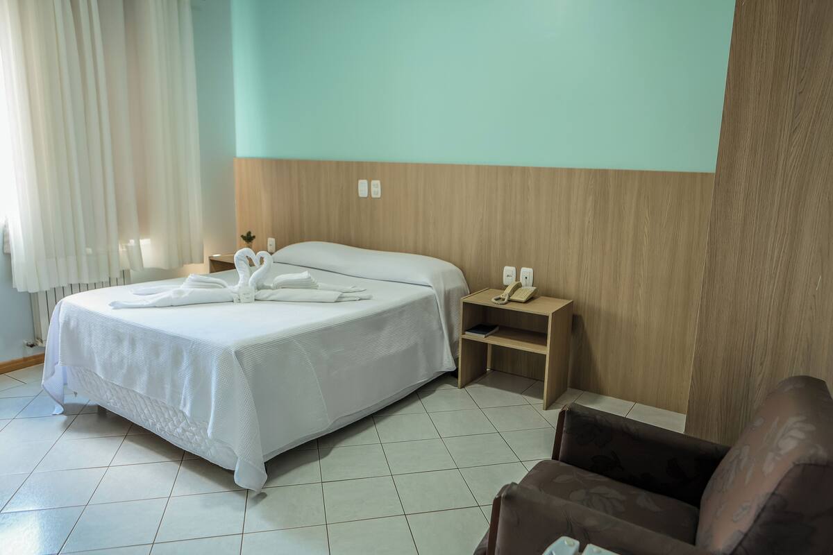 A hotel room with a bed, a bedside table with a phone, and a chair.