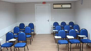 A conference room with rows of blue chairs and white tables, a white door, and a ceiling-mounted air conditioning unit.