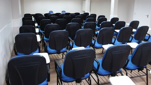 A conference room with rows of blue and black chairs, white tables, and a whiteboard at the front. - Center Hotel (Xanxere)