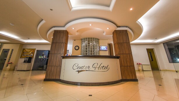 A hotel reception area with a curved reception desk, a clock, and a digital screen on the wall. - Center Hotel (Xanxere)