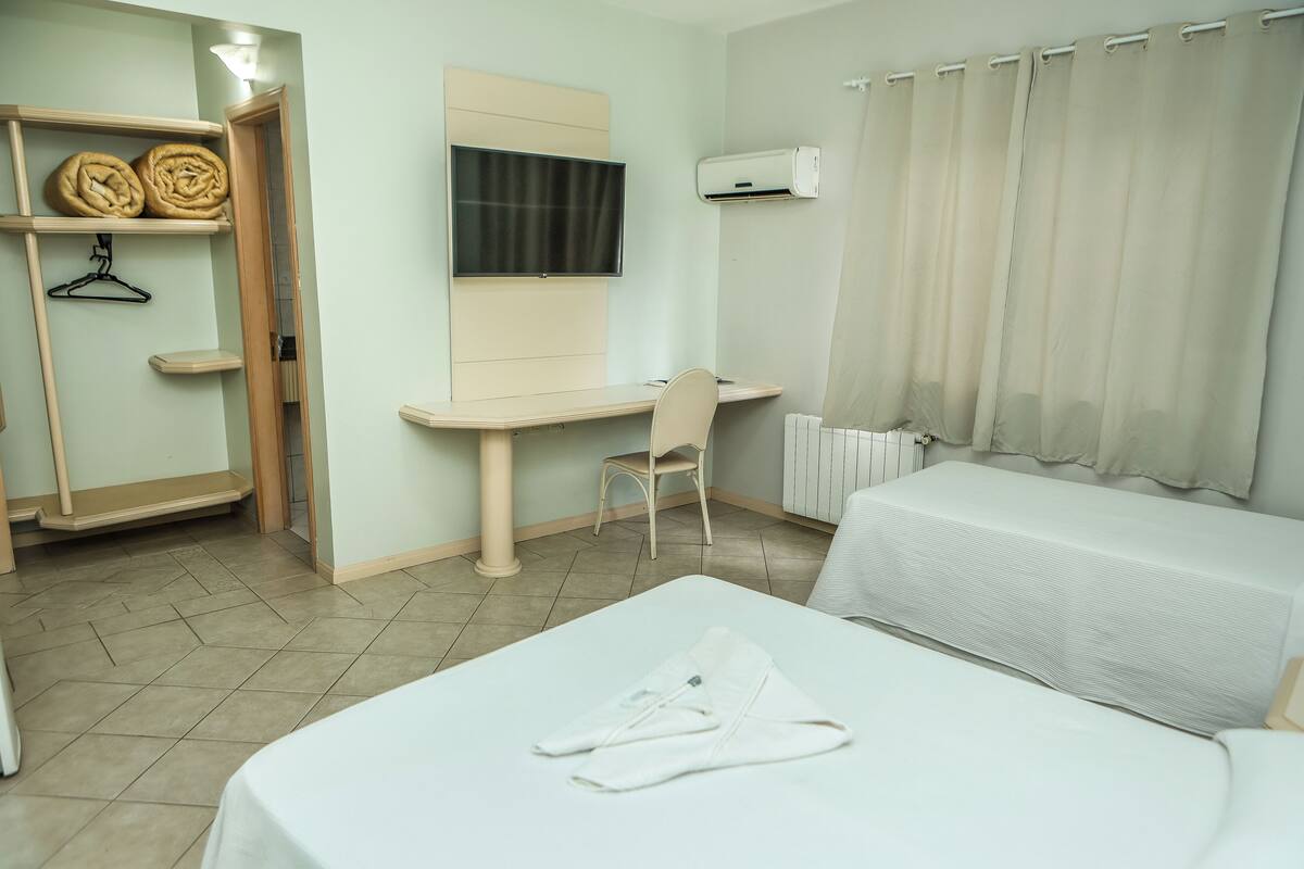 A hotel room with a bed, a desk, a chair, a wardrobe, and a TV.