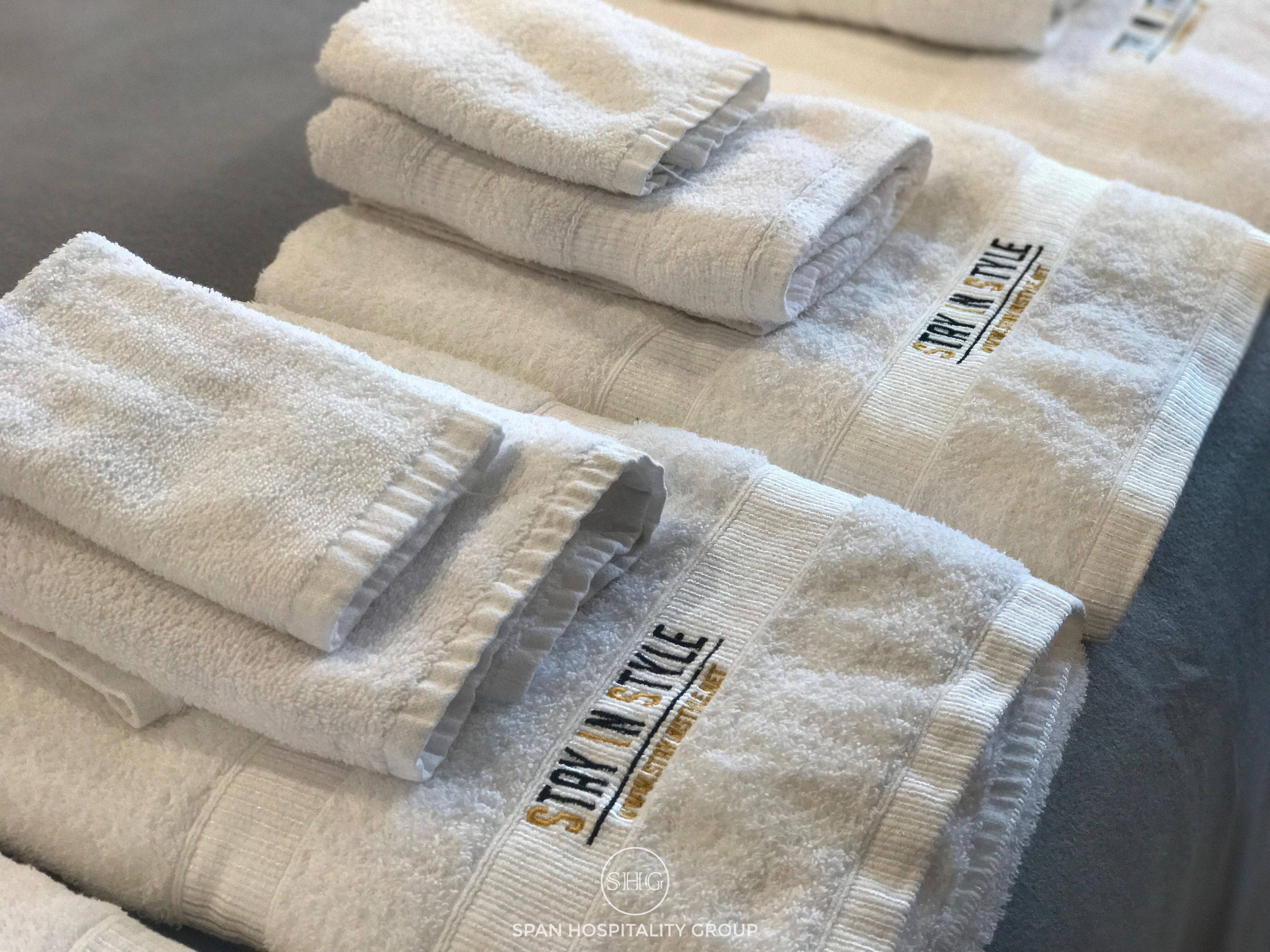 Neatly folded white towels with "STAY IN STYLE" embroidered on them, stacked on a surface.
