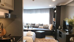 Habitació d'hotel moderna amb cuineta, seients de sofà, una finestra gran amb cortines i vista a la ciutat.