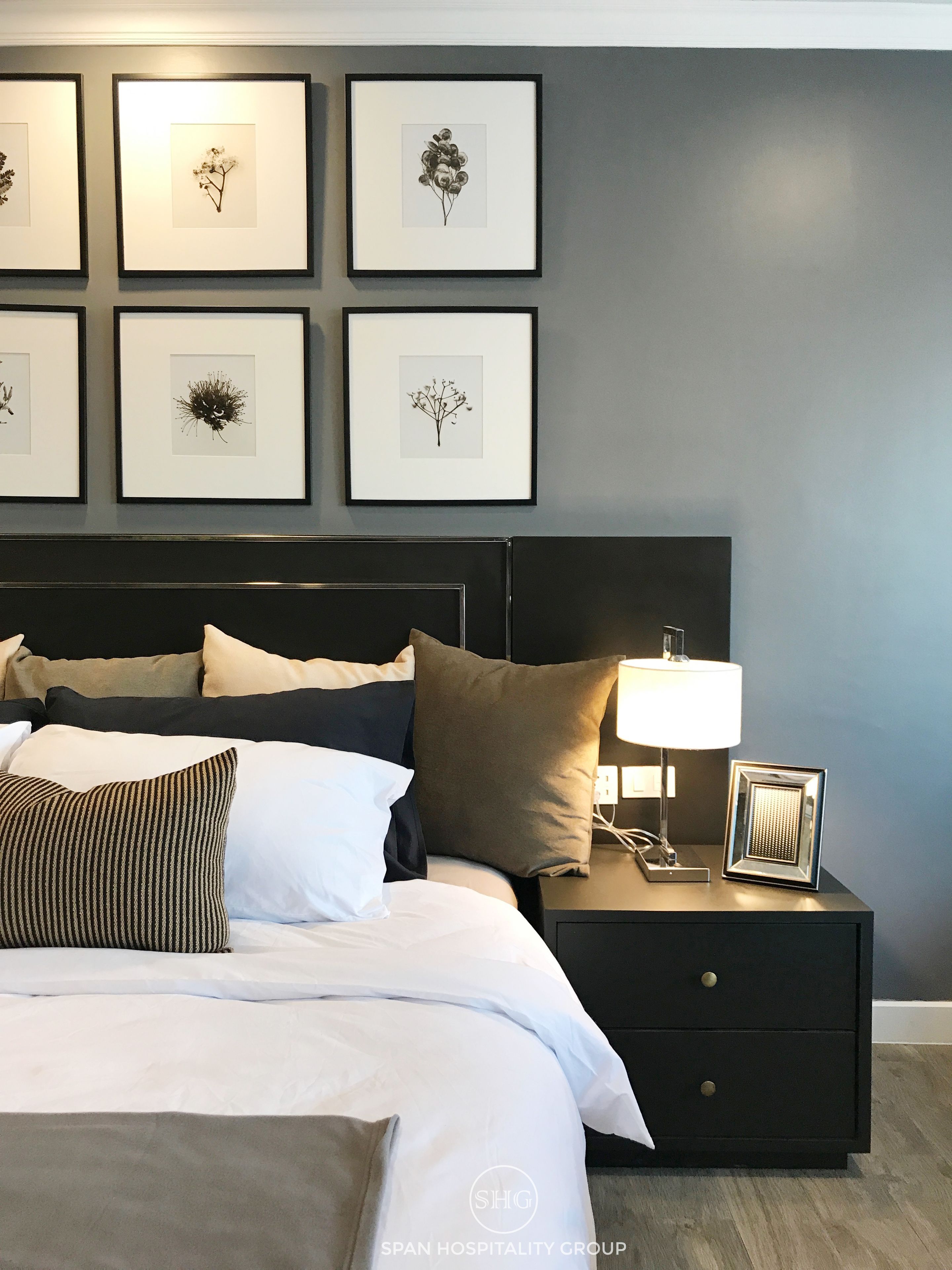 A neatly made bed with white and brown bedding, a black headboard, and a bedside table with a lamp and a framed picture.