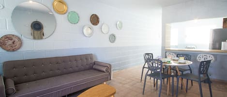 A modern living room with a grey sofa, wooden coffee table, and a dining area with a round table and chairs.