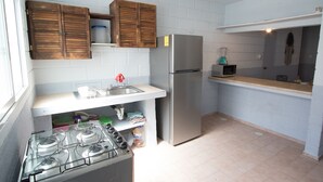 A compact kitchen with a gas stove, a stainless steel refrigerator, wooden cabinets, and a microwave. - Tohoku Townhouse 4 (Playa del Carmen)