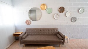 A modern living room with a brown sofa, a wooden coffee table, and a white brick wall adorned with various decorative plates and a mirror. - Tohoku Townhouse 4 (Playa del Carmen)