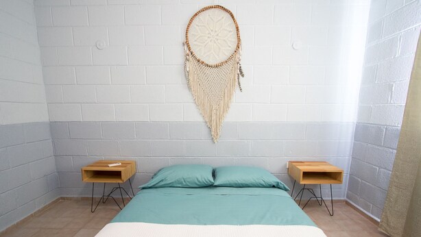 A bedroom with a bed, two nightstands, a wall-mounted dreamcatcher, and a white brick wall. - Tohoku Townhouse 4 (Playa del Carmen)