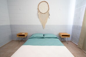 Ein Schlafzimmer mit einem Bett, zwei Nachttischen, einem an der Wand befestigten Traumfänger und einer weißen Ziegelwand.