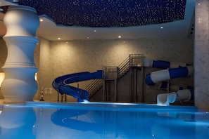 An indoor swimming pool with a starry ceiling, a blue slide, and marble walls.