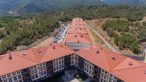 A multi-story hotel with red-tiled roofs, a parking lot, and a mountainous backdrop.