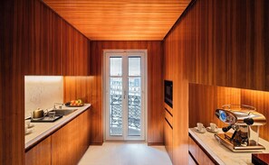 A narrow kitchen with wooden paneling, a window with a view, a coffee machine, and a fruit bowl on the counter.
