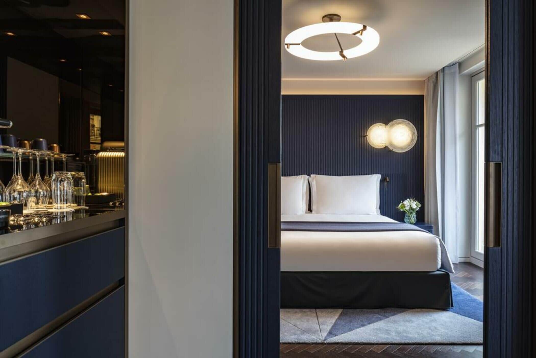 A hotel room with a bed, bedside table, and a view of the city.