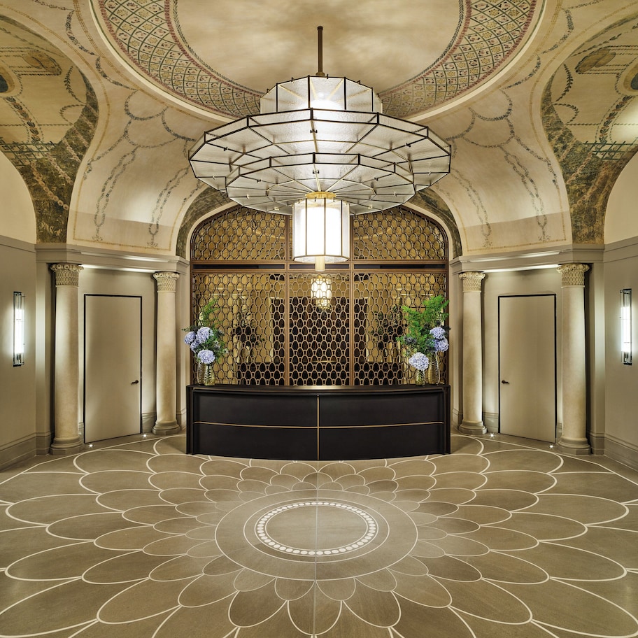 A grand lobby with a decorative ceiling, a central chandelier, and a patterned floor.