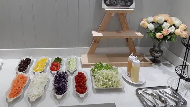 A juice menu board, a variety of fresh vegetables, and a vase of flowers on a table. - Barbados Terrace (Rayong)