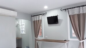 A bedroom with a bed, a desk, a TV, and curtains. - Barbados Terrace (Rayong)