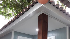 A house with a light blue exterior, white trim, and a wooden porch. There are two potted plants on the porch. - Barbados Terrace (Rayong)